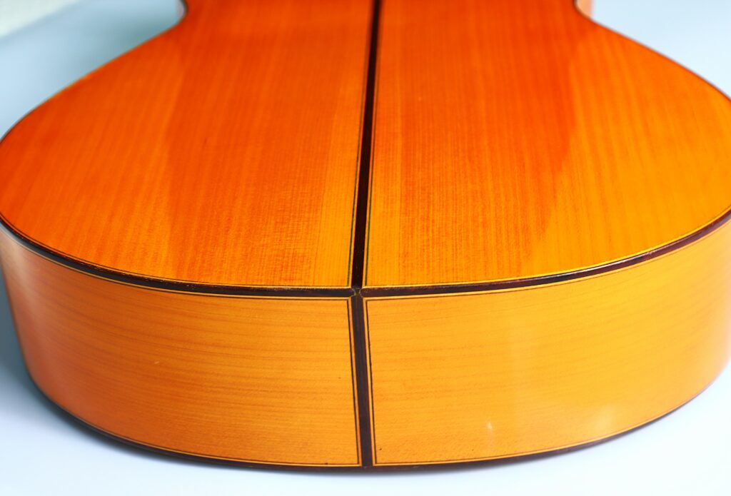 Close-Up Of The Lorenzo Alvarez 1982 Flamenco Guitar’s Glossy Wooden Back, Highlighting The Smooth Finish And Dark Lines That Divide It Into Symmetrical Sections.