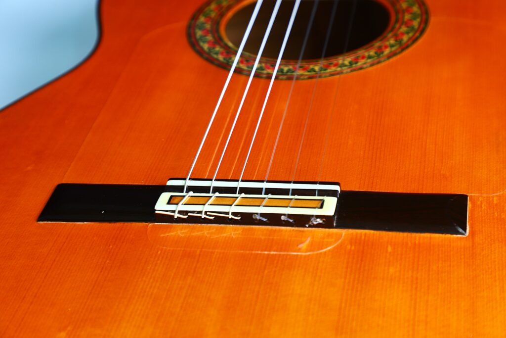 Close-Up Of The Lorenzo Alvarez 1982 Flamenco Guitar’s Bridge And Strings, Highlighting Its Orange Wood Body And Beautifully Decorated Soundhole In The Background.