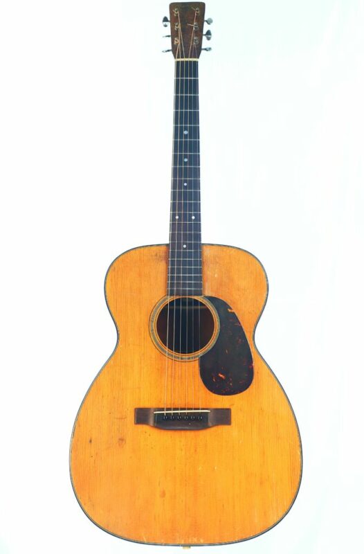 Martin 00-18 1956 acoustic guitar with a natural wood finish, black pickguard, six strings, and visible signs of wear, shown against a plain white background.