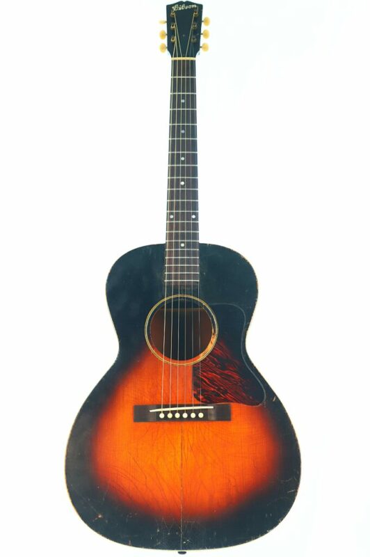 The Gibson L-00 1934 Acoustic Guitar features a sunburst finish, six strings, and a dark pickguard, showcased against a white background.