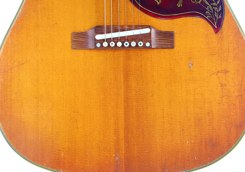 Nahaufnahme Eines Gibson Hummingbird 1966 Akustik Gitarre , Der Den Holzsteg, Die Saiten, Das Florale Schlagbrett Und Die Leichten Kratzer Auf Dem Orange-Braunen Finish Hervorhebt.