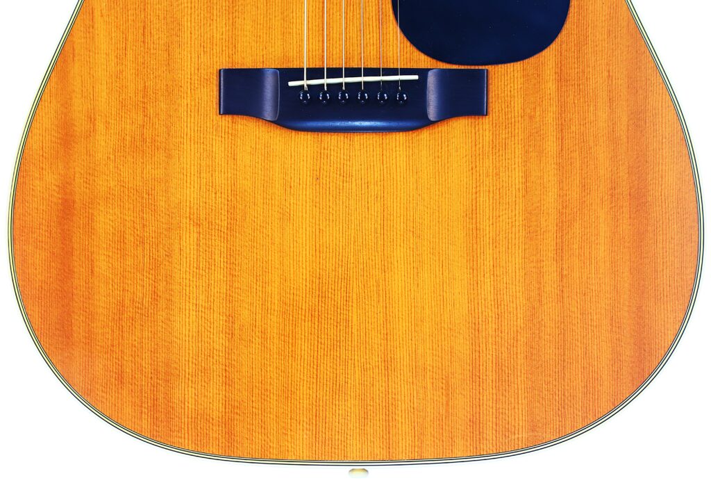 Close-Up Of A Martin D-35 1979 Acoustic Guitar Body, Highlighting Its Wooden Texture, Bridge, Strings, And Black Pickguard Against A White Background.