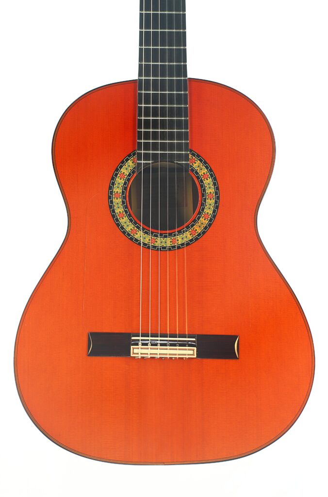 Eine Flamenco-Gitarre „Paco de Lucia Spezial“ von Hermanos Conde aus dem Jahr 1998 mit rotbraunem Korpus, einer dekorativen Rosette um das Schallloch, sechs Saiten und einem dunklen Griffbrett, abgebildet vor weißem Hintergrund. Eine Flamenco-Gitarre „Paco de Lucia Spezial“ von Hermanos Conde aus dem Jahr 1998 mit rotbraunem Korpus, einer dekorativen Rosette um das Schallloch, sechs Saiten und einem dunklen Griffbrett, abgebildet vor weißem Hintergrund.