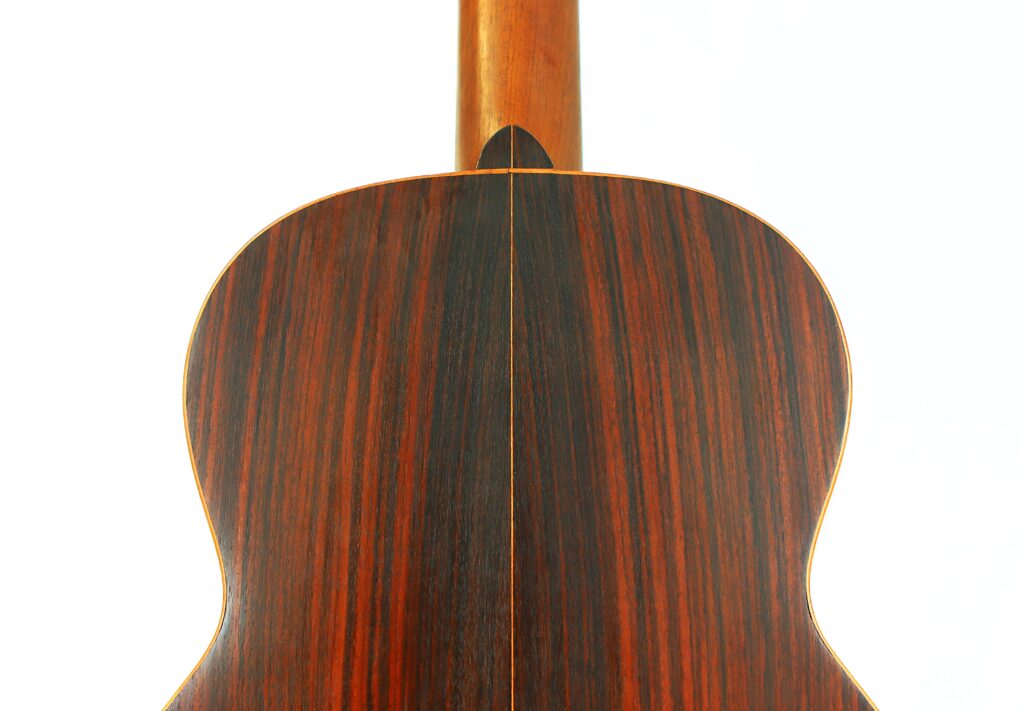 The Back Of A Salvador Ibanez ~1900 Classical Guitar Made From Dark Wood With Reddish-Brown And Black Vertical Grain Patterns, Photographed Against A Plain White Background.