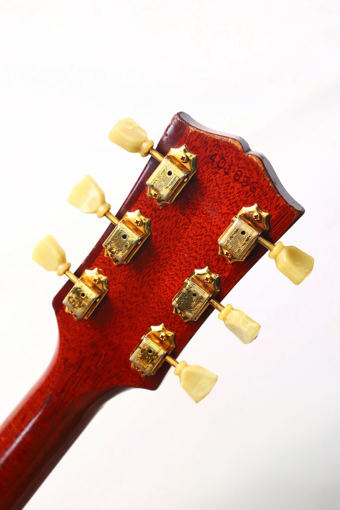 Nahaufnahme Der Rückseite Einer Gibson Hummingbird 1966 Akustik Gitarre Mit Sechs Goldenen Stimmwirbeln Mit Cremefarbenen Knöpfen Auf Einem Rotbraunen Holzfinish Vor Einem Schlichten Weißen Hintergrund.