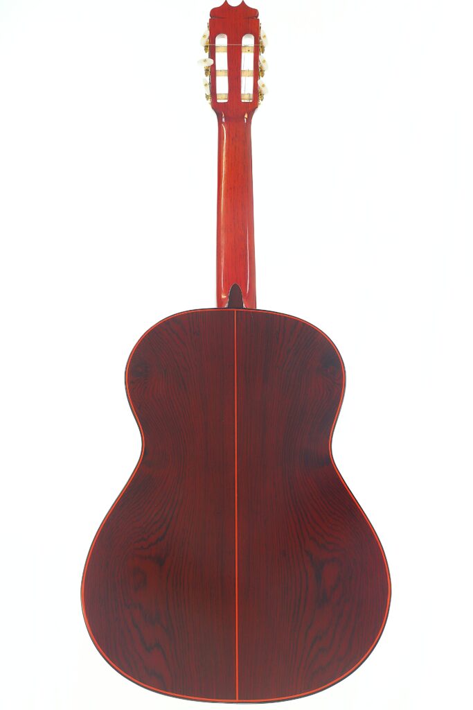 Das Bild zeigt die Rückansicht einer „Hermanos Conde 1998 Paco de Lucia Spezial Flamenco“-Gitarre mit einer satten, dunkelrot-braunen Holzoberfläche, deren Maserung deutlich zu erkennen ist, sowie einer glänzenden Oberfläche. Das Instrument, das die für Hermanos-Conde-Gitarren charakteristische, renommierte Handwerkskunst verkörpert, wurde vor einem weißen Hintergrund fotografiert. Das Bild zeigt die Rückansicht einer „Hermanos Conde 1998 Paco de Lucia Spezial Flamenco“-Gitarre mit einer satten, dunkelrot-braunen Holzoberfläche, deren Maserung deutlich zu erkennen ist, sowie einer glänzenden Oberfläche. Das Instrument, das die für Hermanos-Conde-Gitarren charakteristische, renommierte Handwerkskunst verkörpert, wurde vor einem weißen Hintergrund fotografiert.