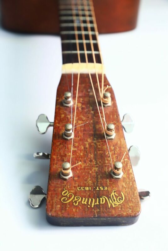 Nahaufnahme der Kopfplatte einer Westerngitarre mit Stimmwirbeln, Saiten und dem Martin & Co.-Logo mit "Est. 1833" in goldener Schrift auf der Holzoberfläche.