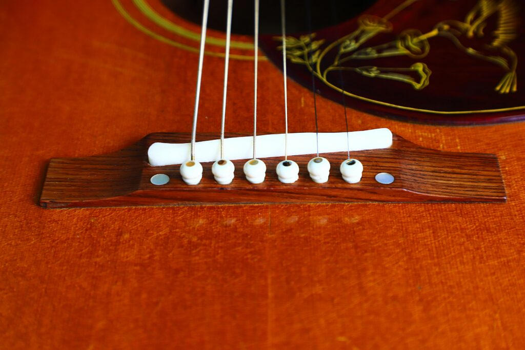 Nahaufnahme Einer Gibson Hummingbird 1966 Akustik Gitarre Mit Sechs Weißen Stegstiften, Saiten Und Einem Teil Des Dekorativen Schlagbretts Auf Einem Warmbraunen Holzkorpus.