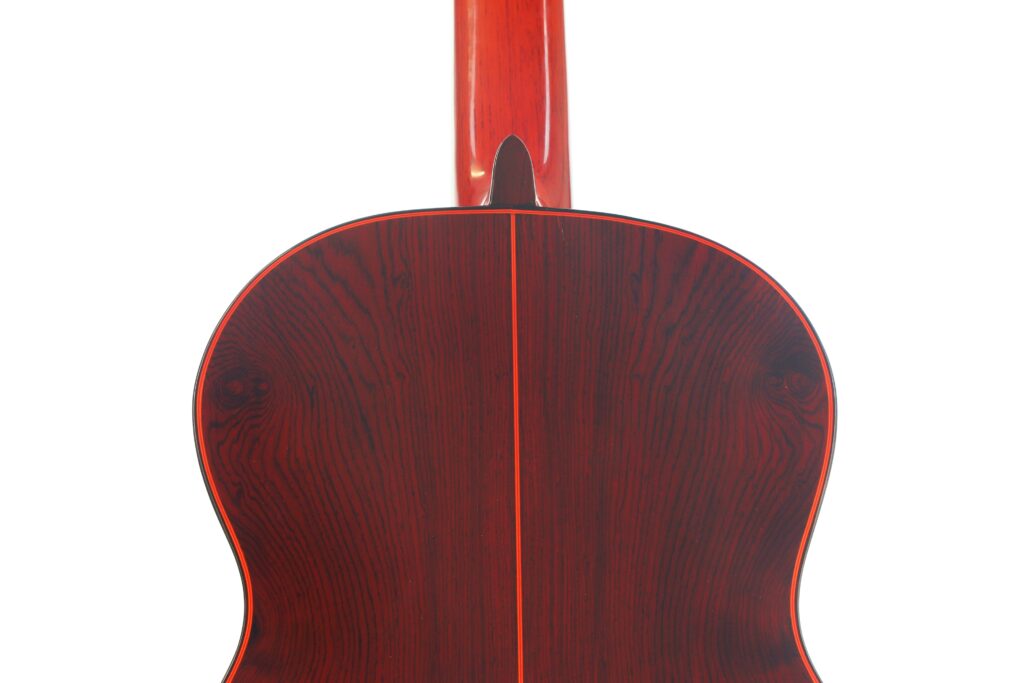 Die Rückseite einer „Hermanos Conde 1998 Paco de Lucia Spezial Flamenco“-Gitarre mit einer dunklen, rotbraunen Lackierung und sichtbarer Maserung ist aufrecht vor einem weißen Hintergrund abgebildet. Die Rückseite einer „Hermanos Conde 1998 Paco de Lucia Spezial Flamenco“-Gitarre mit einer dunklen, rotbraunen Lackierung und sichtbarer Maserung ist aufrecht vor einem weißen Hintergrund abgebildet.