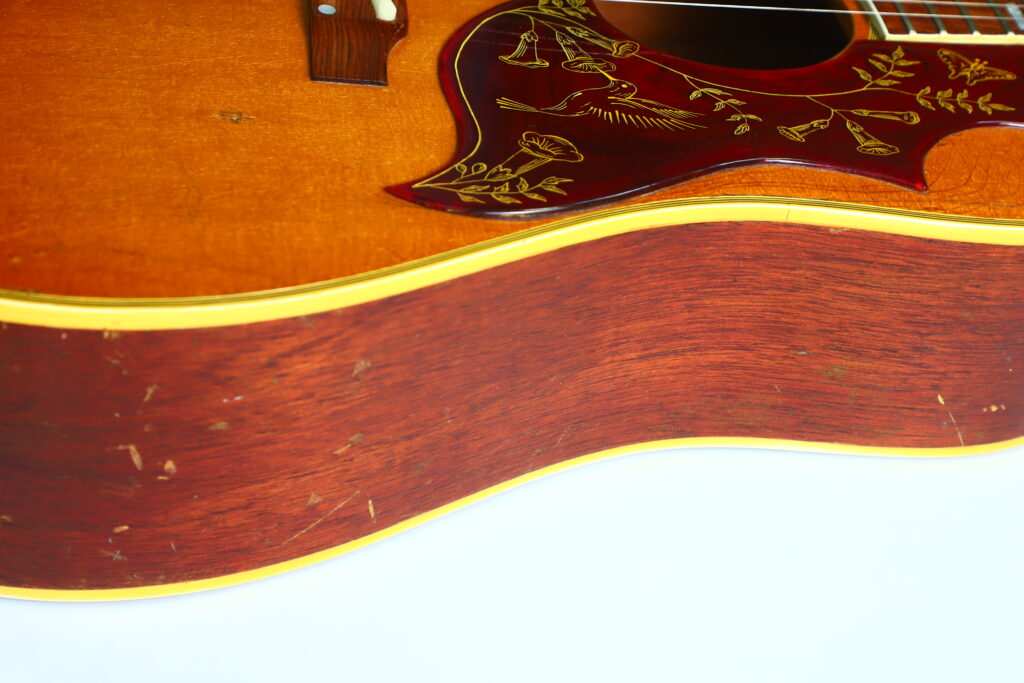 Nahaufnahme Eines Gibson Hummingbird 1966 Akustik Gitarre Mit Holzmaserung, Floral Gemustertem Schlagbrett Und Gelbem Rand Auf Weißem Hintergrund.
