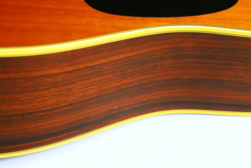 Close-Up Of The Side Of A Martin D-35 1979 Acoustic Guitar, Highlighting Its Wood Grain, Yellow Edging, And Curved Body Against A White Background.