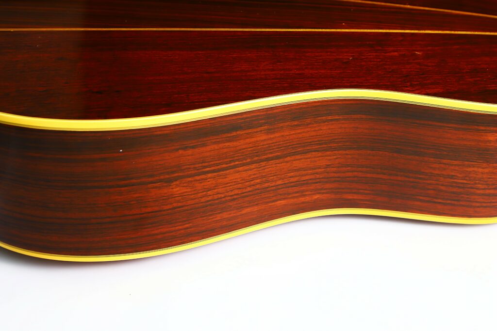 Close-Up Of The Side Of A Martin D-35 1979 Acoustic Guitar, Highlighting Its Polished Wood Grain And Yellow Trim Against A White Background.