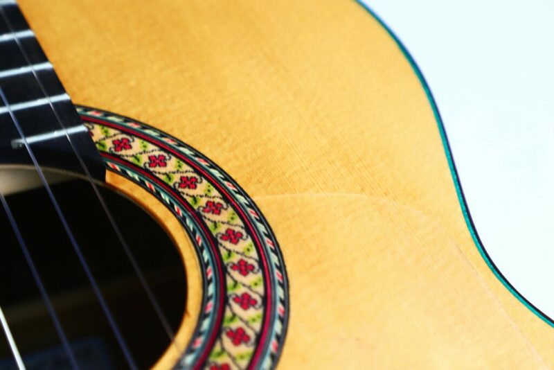 Close-up of the Sergio Sanchez 2024 Negra Flamenco Guitar’s body, highlighting the colorful floral rosette around the sound hole, with part of the strings and frets visible on the left.