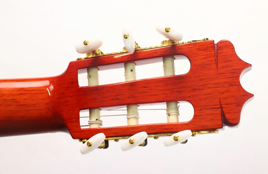 Nahaufnahme des Kopfstücks einer „Hermanos Conde 1998 Paco de Lucia Spezial Flamenco“-Gitarre, bei der die Stimmwirbel und Saiten vor dem Hintergrund einer polierten Holzoberfläche und eines schlichten weißen Hintergrunds hervorgehoben sind. Nahaufnahme des Kopfstücks einer „Hermanos Conde 1998 Paco de Lucia Spezial Flamenco“-Gitarre, bei der die Stimmwirbel und Saiten vor dem Hintergrund einer polierten Holzoberfläche und eines schlichten weißen Hintergrunds hervorgehoben sind.