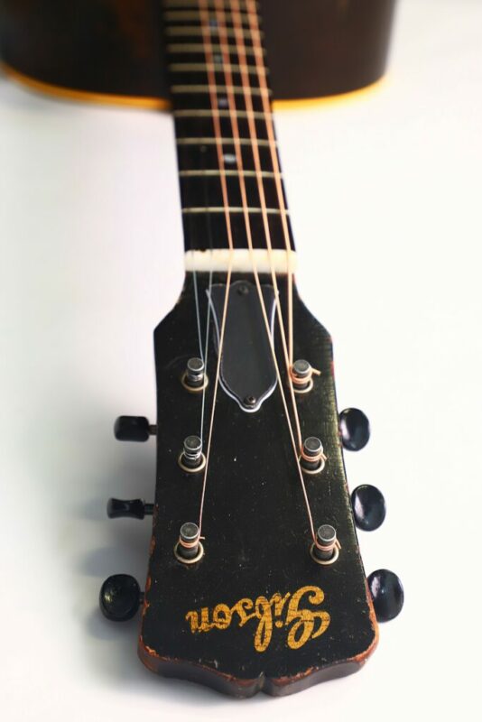 Close-up of the headstock and upper neck of the Gibson LG-2 1946 Acoustic Guitar, featuring six tuning pegs and a gold Gibson logo on dark wood, with strings leading toward the body against a white background.