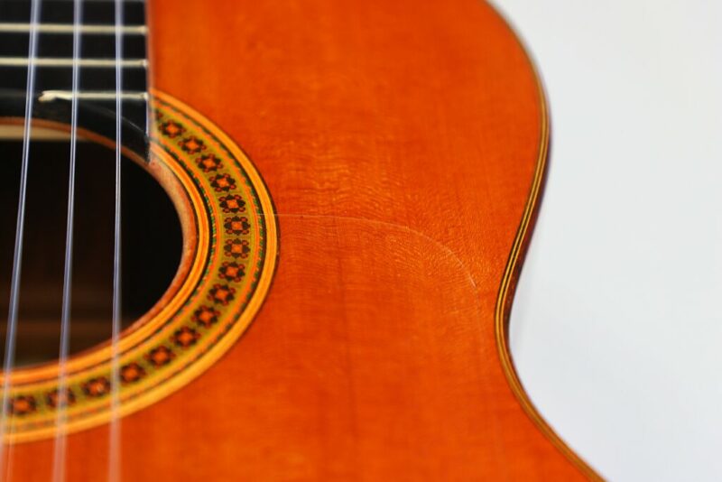Nahaufnahme des Holzkorpus einer Akustikgitarre. Zu sehen sind das Schallloch, ein Teil der Rosettenverzierung, die Saiten und ein sichtbarer Riss, der in der Nähe der Kante durch das Holz verläuft.