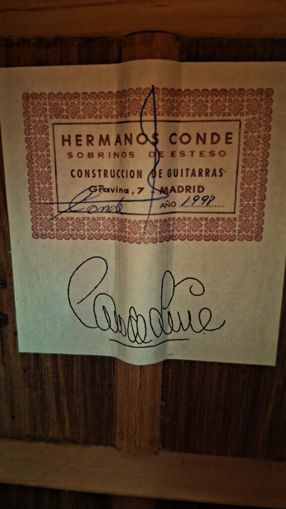 Eine Nahaufnahme des Gitarrenetiketts mit der Aufschrift „Hermanos Conde Sobrinos de Esteso, Construcción de Guitarras, Madrid“, das handschriftliche Unterschriften und das Datum 1998 trägt, unterstreicht die Handwerkskunst und das Vermächtnis der Gitarrenbauer von Hermanos Conde, die in der „Hermanos Conde 1998 Paco de Lucia Spezial Flamenco-Gitarre“ zum Ausdruck kommen. Eine Nahaufnahme des Gitarrenetiketts mit der Aufschrift „Hermanos Conde Sobrinos de Esteso, Construcción de Guitarras, Madrid“, das handschriftliche Unterschriften und das Datum 1998 trägt, unterstreicht die Handwerkskunst und das Vermächtnis der Gitarrenbauer von Hermanos Conde, die in der „Hermanos Conde 1998 Paco de Lucia Spezial Flamenco-Gitarre“ zum Ausdruck kommen.
