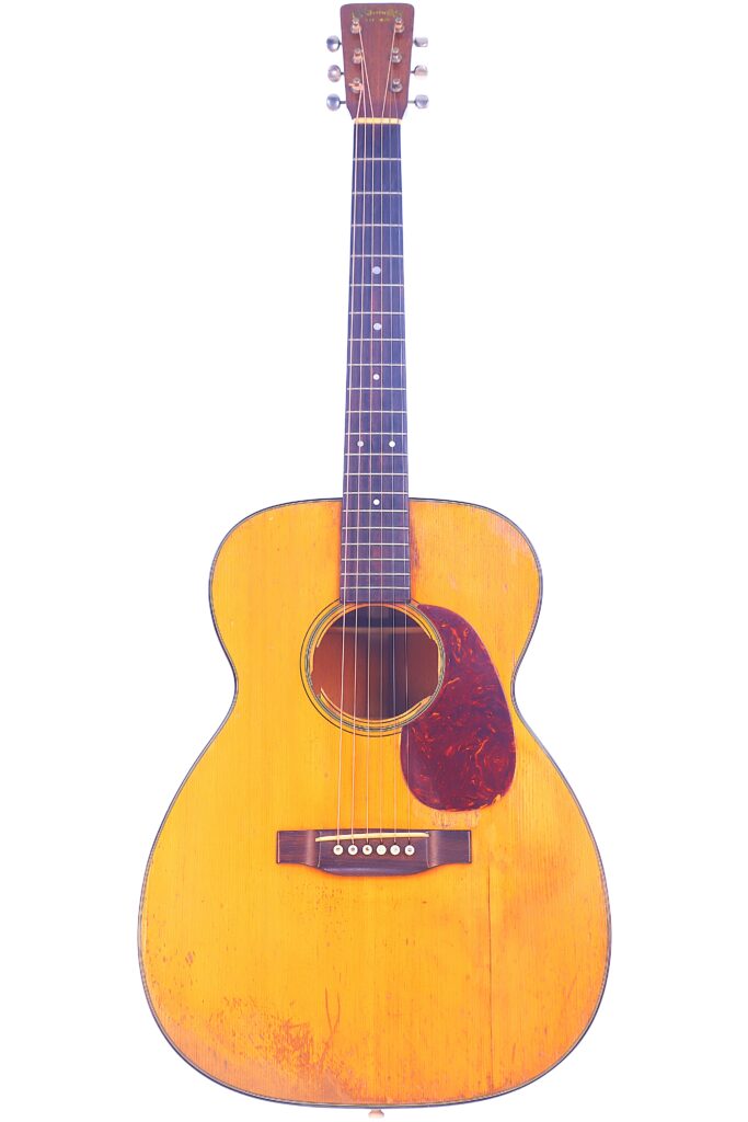 The Martin 00-18 1952 Acoustic Guitar Features A Light Wood Body, Dark Pickguard, Six Strings, And Dot Inlays On The Fingerboard, Displayed Against A White Background.