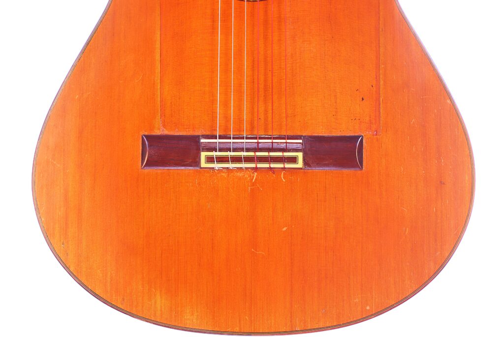 Close-Up Of The Lower Half Of A Jose Ramirez 1968 Flamenco Guitar, Featuring Its Warm, Orange-Brown Wooden Body With Visible Grain And Minor Scratches, Along With The Bridge And Strings.