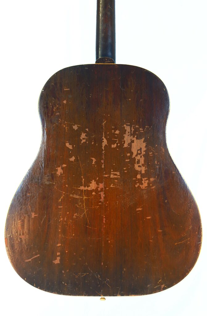 A Close-Up Of The Back Of A Gibson J-45 1951 Acoustic Guitar Shows Its Dark Wooden Finish With Noticeable Scratches, Scuffs, And Worn Areas That Highlight Heavy Use And Vintage Character.