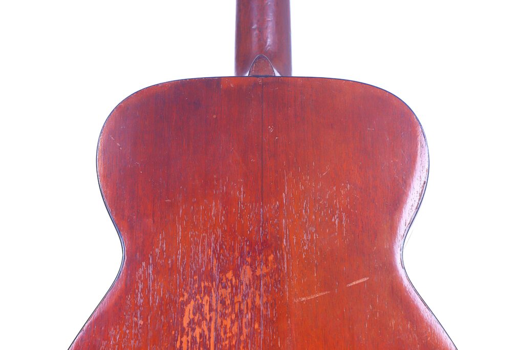 Close-Up Of The Back Of A Martin 00-18 1952 Acoustic Guitar With A Reddish-Brown Wood Finish, Showing Visible Scratches And Wear. The Well-Lit Image Features A White Background.