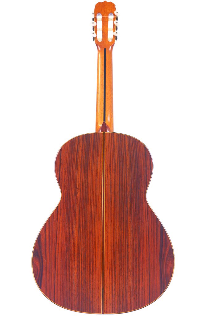 The Back View Of A Jose Ramirez 1A 1975 Classical Guitar Reveals A Glossy Wooden Finish With Dark And Light Brown Streaks And A Vertical Center Seam Running Down The Body.