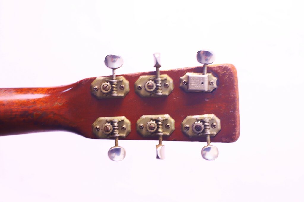 Close-Up Of The Back Of A Martin 00-18 1953 Acoustic Guitar Headstock, Featuring Six Metal Tuning Pegs And Keys Against A White Background. The Worn Wood Displays A Rich, Reddish-Brown Finish.