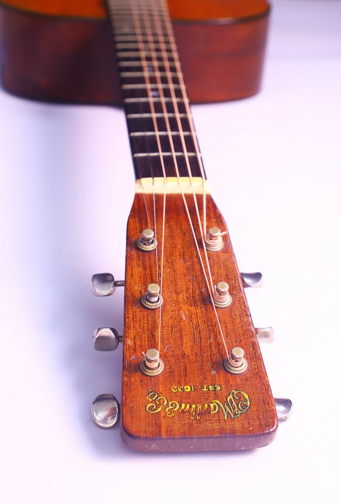 Close-Up Of The Headstock And Tuning Pegs Of A Martin 00-18 1953 Acoustic Guitar, Featuring Martin &Amp; Co. Est. 1833 In Yellow On The Wood, Set Against A Plain White Background.