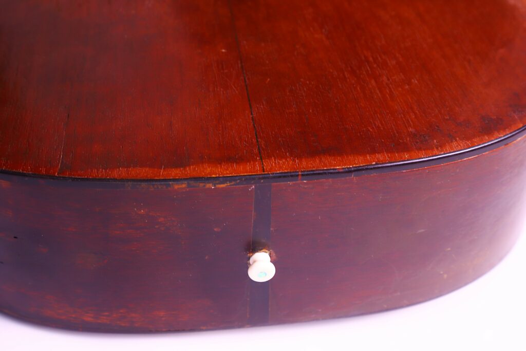 Close-Up Of The Bottom Side Of A Martin 00-18 1953 Acoustic Guitar, Featuring A Fine Vertical Crack Along The Center And A White Strap Button Near The Edge.