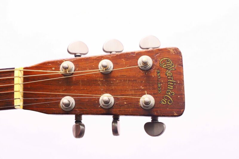 Close-Up Of The Martin 00-18 1954 Acoustic Guitar’s Wooden Headstock With Six Tuning Pegs And Engraved Martin &Amp; Co Logo, Set Against A Plain White Background.