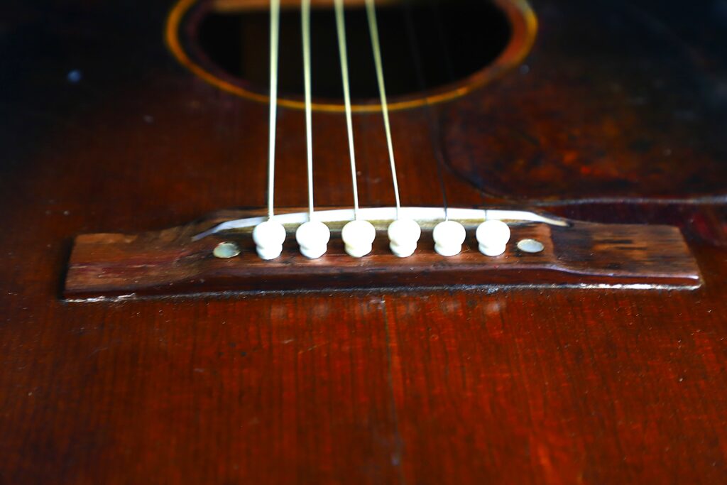 Close-Up Of The Bridge And Strings On A Gibson J-45 1951 Acoustic Guitar, Highlighting The White Bridge Pins And Part Of Its Glossy Wooden Body.