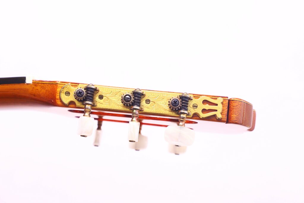 Close-Up Of A Jose Ramirez 1A 1975 Classical Guitar Headstock With Three White Tuning Pegs, An Ornate Brass Tuning Plate, And Wooden Finish Against A Plain White Background.