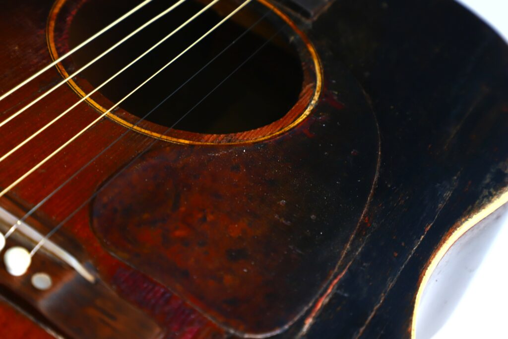 Close-Up Of A Vintage Gibson J-45 1951 Acoustic Guitar, Featuring Its Sound Hole, Strings, And A Dark, Scratched Pickguard With Visible Signs Of Age And Use.