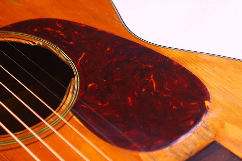 Close-Up Of A Martin 00-18 1953 Acoustic Guitar, Highlighting Its Strings, Soundhole, And Marbled Reddish-Brown Pickguard Set Against The Wooden Body.