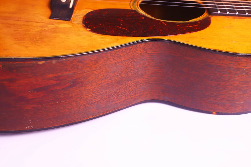 Close-Up Of The Side And Top Of A Martin 00-18 1953 Acoustic Guitar, Highlighting Its Wooden Body, Strings, And Pickguard Against A White Background.