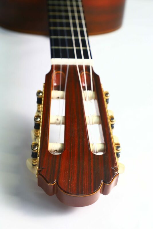 Nahaufnahme Der Kopfplatte Einer Masaru Kohno Concert 1982 Konzertgitarre Mit Stimmwirbeln, Nylonsaiten Und Holzmaserungen, Wobei Der Hals Auf Einer Weißen Fläche In Den Hintergrund Ragt.