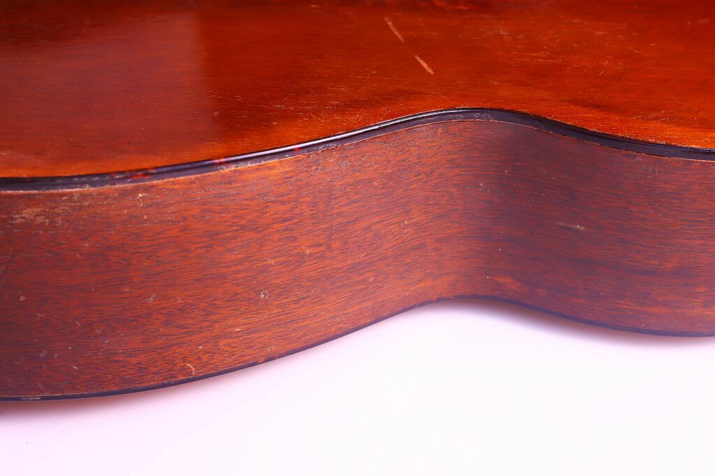 Close-Up Of The Wooden Side And Body Of The Martin 00-18 1953 Acoustic Guitar, Highlighting Its Glossy Brown Finish And Elegant Contours Against A White Background.