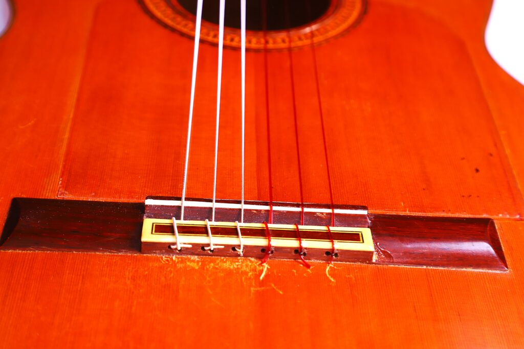 Close-Up Of A Jose Ramirez 1968 Flamenco Guitar, Featuring Part Of The Wooden Body, Bridge, And Strings In Warm Lighting That Highlights The Rich Brown And Orange Wood Tones.