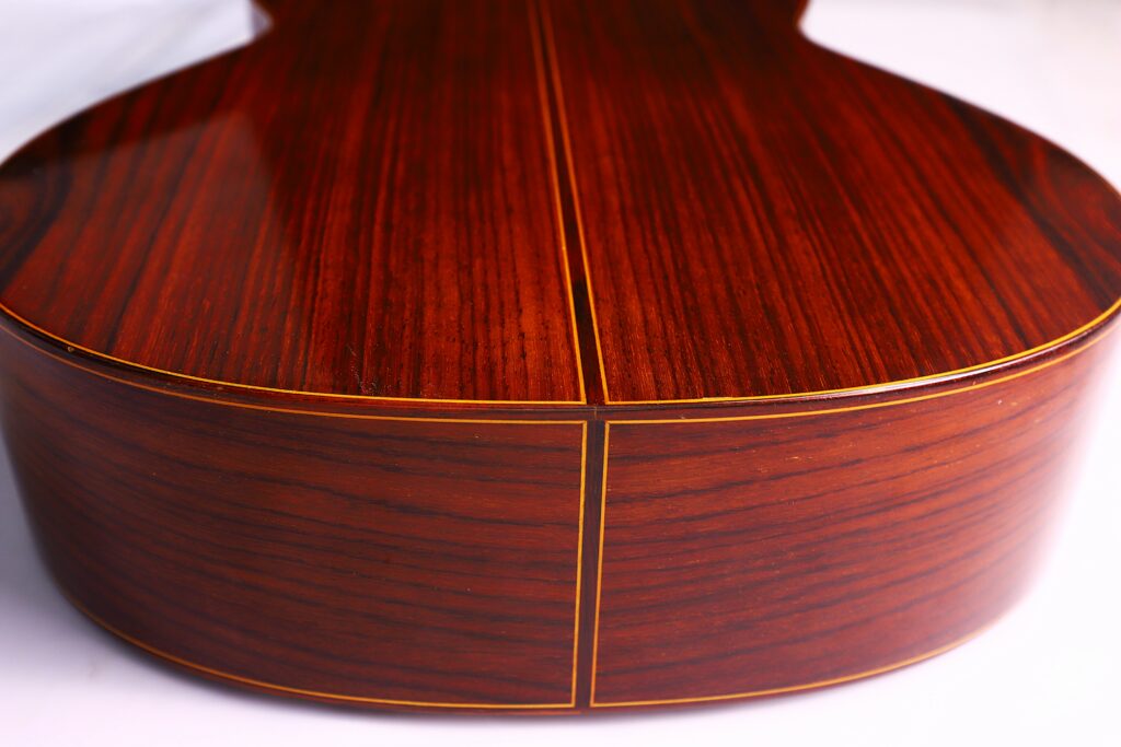Close-Up Of The Back Of A Jose Ramirez 1A 1975 Classical Guitar, Highlighting Its Polished Dark Wood Finish, Fine Parallel Grain Lines, And Elegant Yellow Inlay Detail Along The Seams.