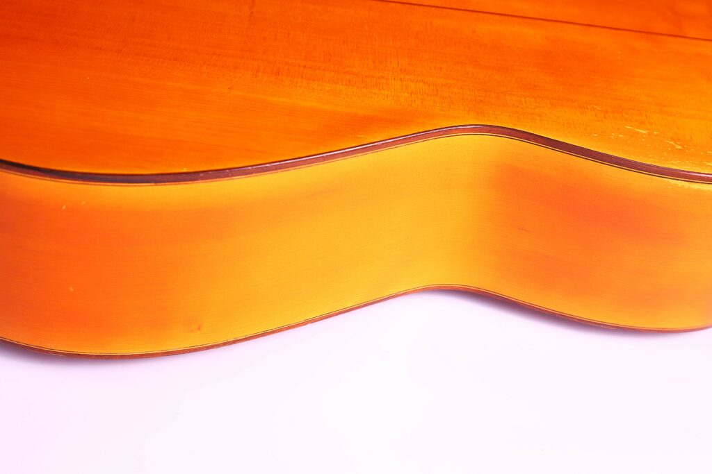 Close-Up Of The Side And Body Of A Jose Ramirez 1968 Flamenco Guitar, Highlighting Its Smooth, Glossy Orange-Brown Finish Against A White Background.