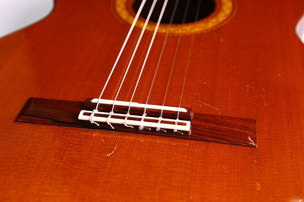Close-Up Of The Strings And Bridge On A Jose Ramirez 1A 1975 Classical Guitars Polished Wooden Body, With Part Of The Sound Hole Visible Near The Top Of The Image.