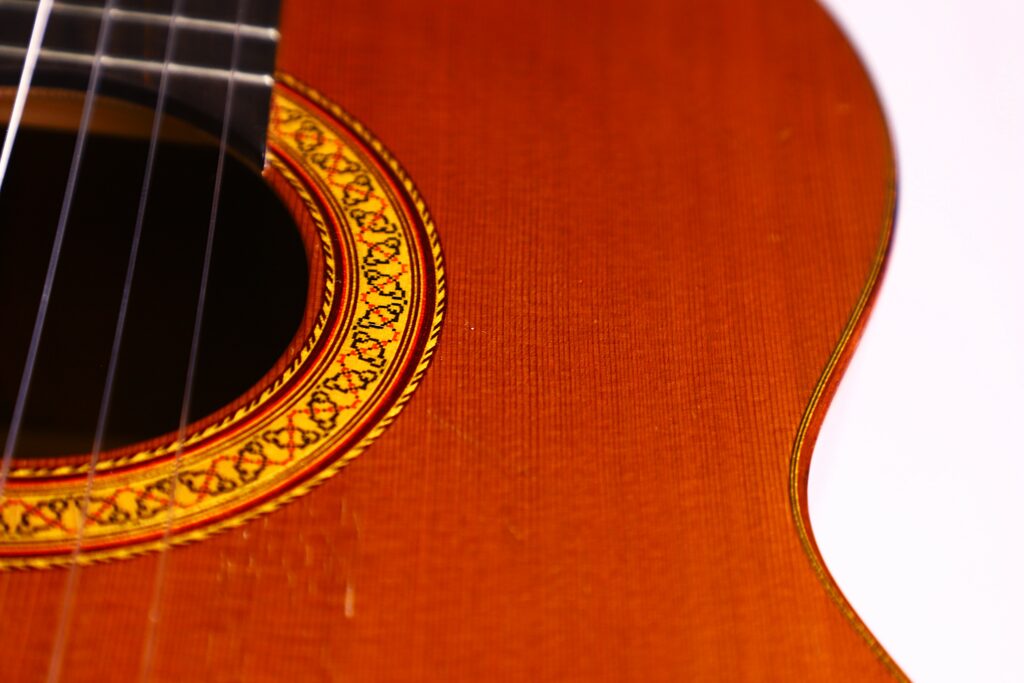 Close-Up Of A Jose Ramirez 1A 1975 Classical Guitar, Highlighting The Sound Holes Intricate Decorative Patterns, Wooden Body, And Guitar Strings On The Left Side; Set Against A White Background.