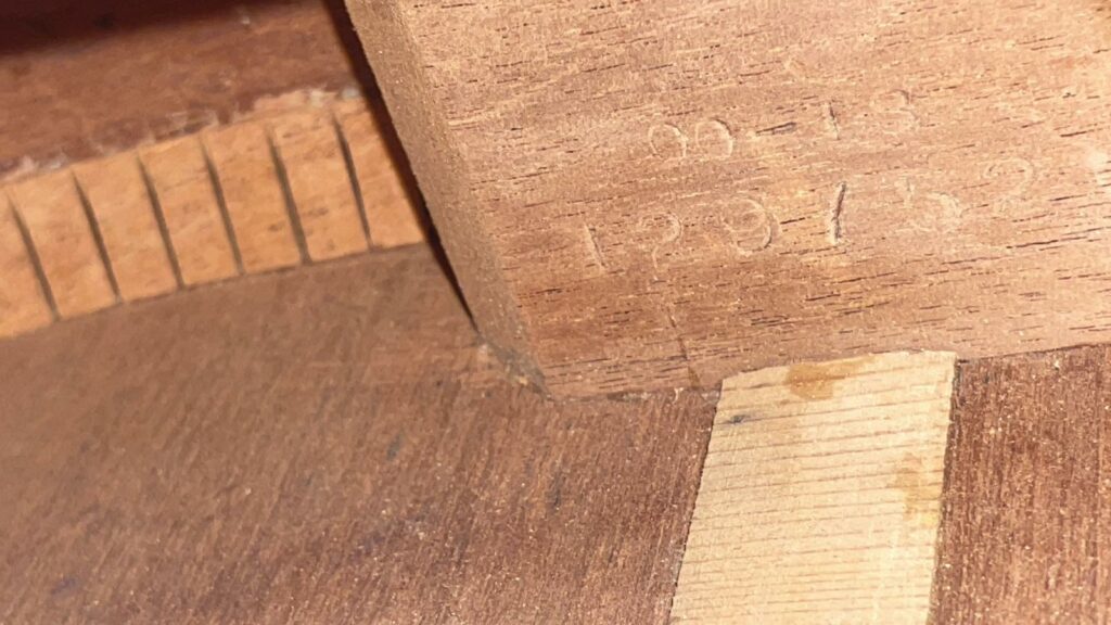 Close-Up Of The Unfinished Wood From A Martin 00-18 1953 Acoustic Guitar Shows A Notched Edge, A Lighter Rectangular Wooden Piece, And Faint Engraved Numbers Or Markings On The Surface.