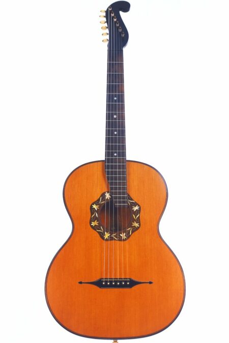 The Stauffer Style 1931 Romantic Guitar features a light brown body, dark fretboard, ornate floral sound hole design, and uniquely shaped headstock, displayed on a plain white background.