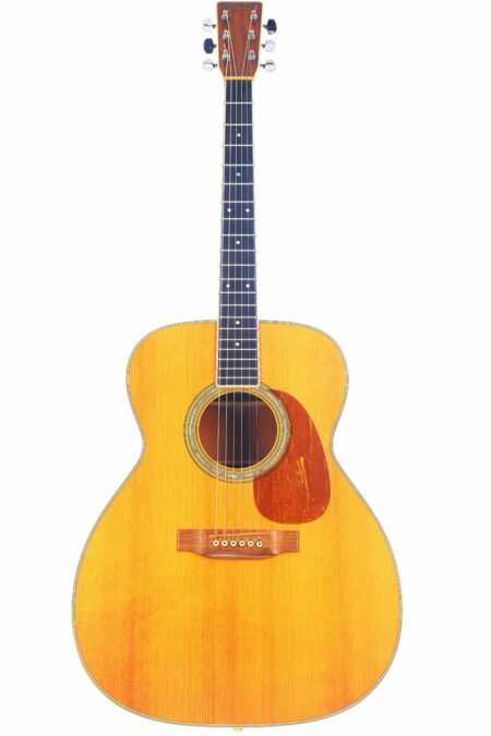 The Martin M-38 1979 Acoustic Guitar features a light wood finish, dark fretboard, six strings, and a reddish-brown pickguard, shown against a white background.