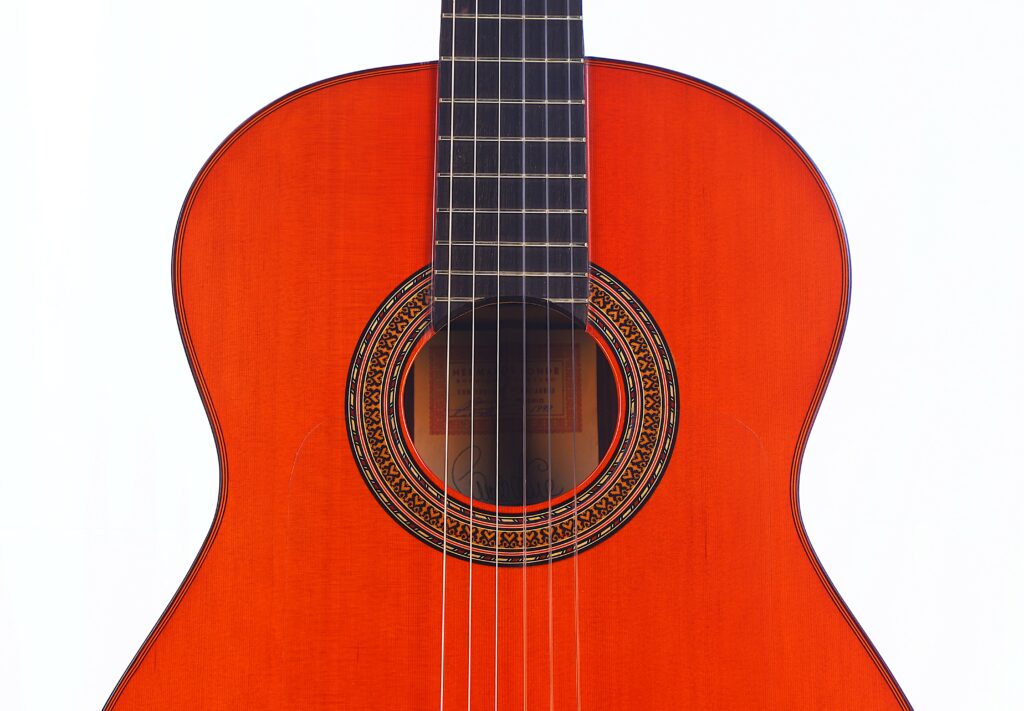Close-Up Of The Hermanos Conde 1999 Paco De Lucia Special Flamenco Guitar, Showing Its Reddish-Brown Body, Strings, And Decorative Rosette Around The Sound Hole, Set Against A White Background.