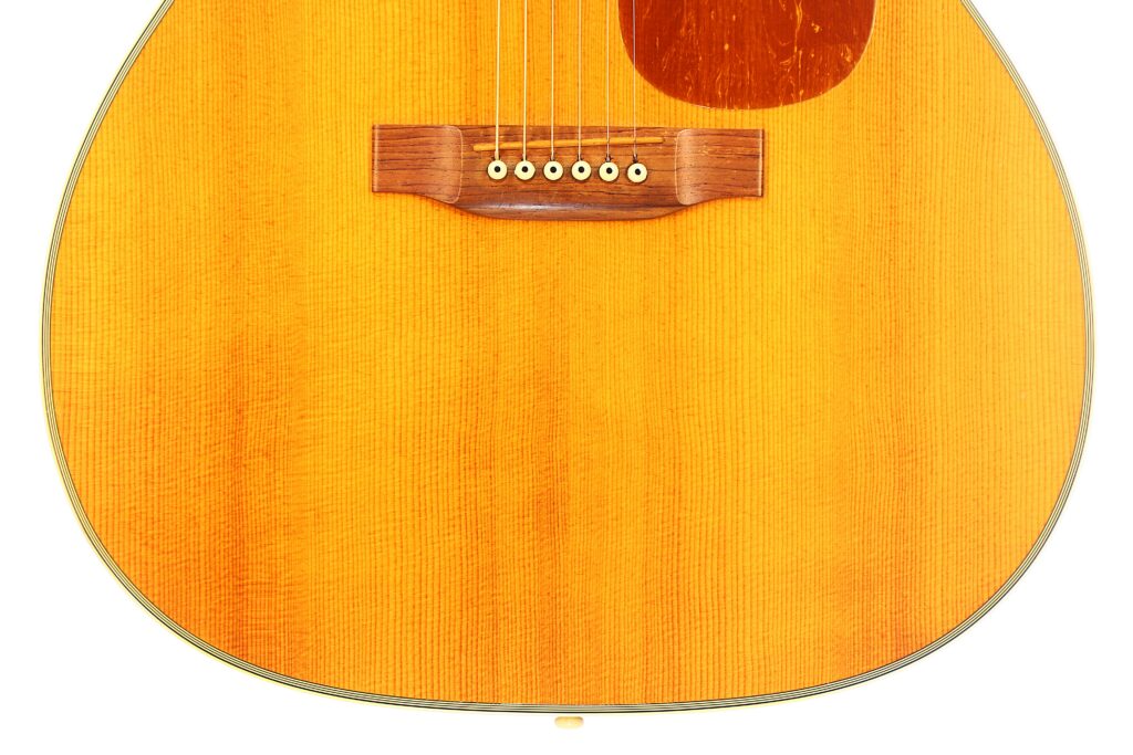 Close-Up Of The Lower Half Of A Martin M-38 1979 Acoustic Guitar, Highlighting The Wooden Bridge, Strings, Pickguard, And The Grain Of Its Light-Colored Wood Body.