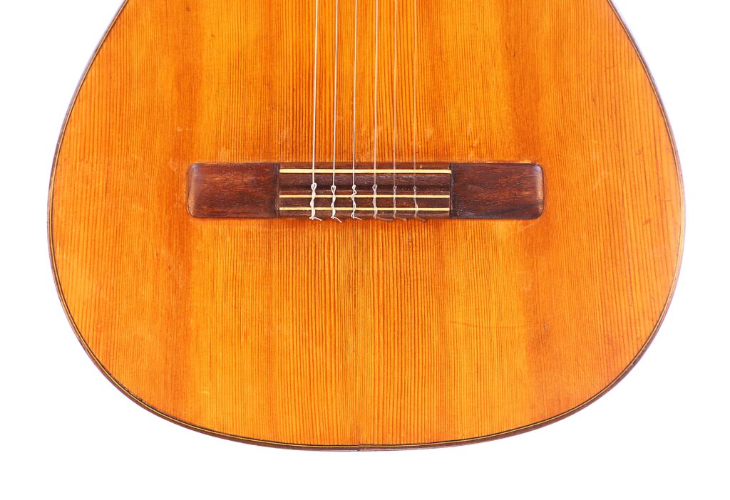 Close-Up Of The Augustin Gaspar Cebrian 1935 Classical Guitar Body, Displaying Its Wooden Surface, Bridge, And Strings Set Against A White Background.
