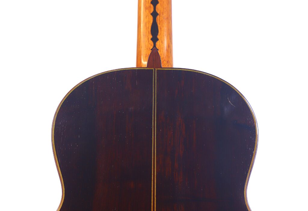 The Image Shows The Back Of A José Ruiz Pedregosa 2020 Classical Guitar With A Polished Dark Wood Finish, Central Inlay Stripe, And Light-Colored Neck With Decorative Black Design, Set Against A White Background.