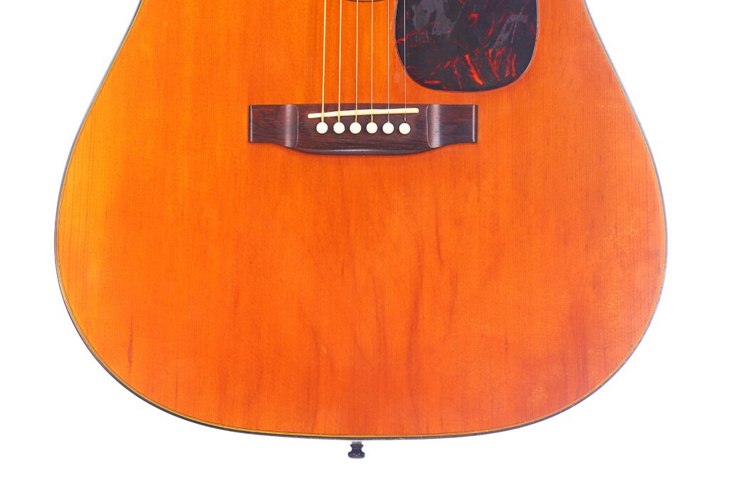Close-Up Of The Lower Half Of A Martin D-18 1967 Acoustic Guitar, Highlighting Its Orange-Brown Wooden Body, Bridge, Strings, And Pickguard Against A White Background.